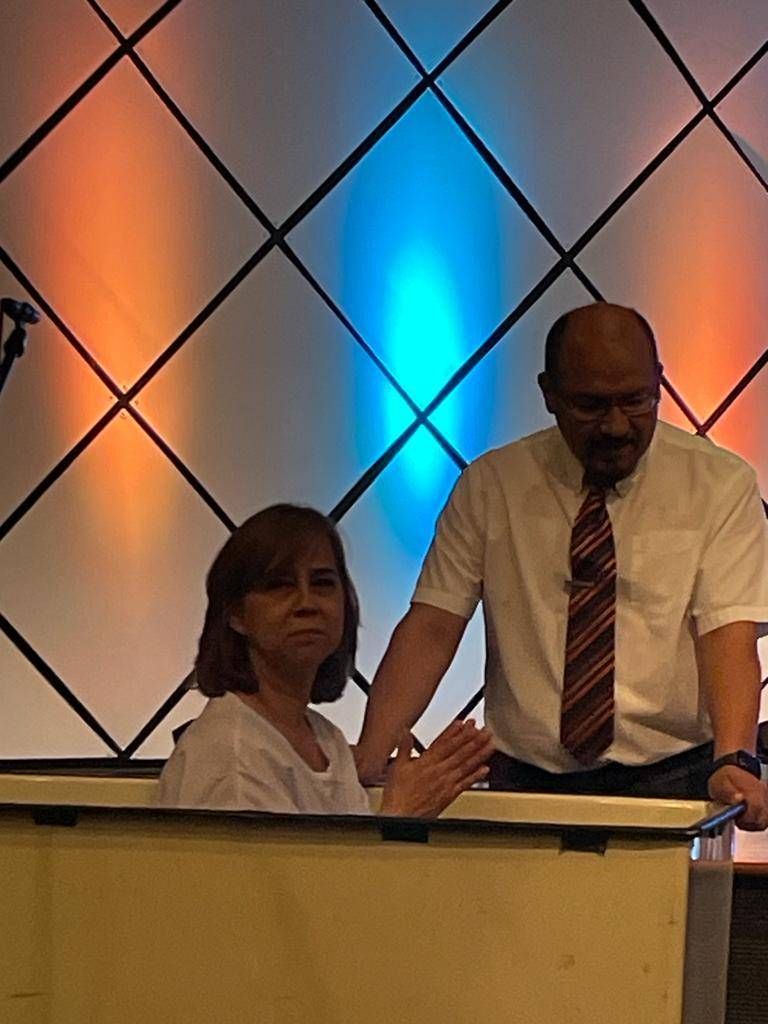 Woman in baptismal, being assisted by a man; church setting with blue and orange backdrop.