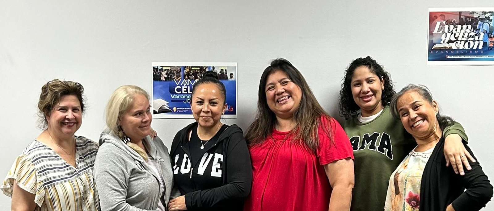 Six smiling people pose against a white wall.