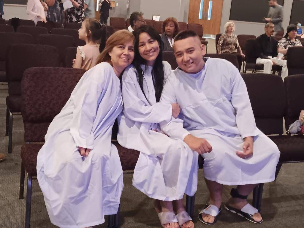 Three people in white robes pose for a photo in a church.