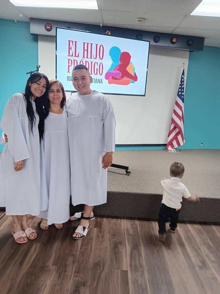Three people in white robes pose in front of a screen displaying 