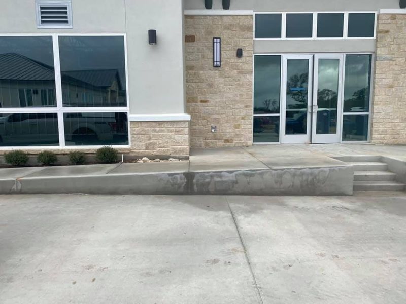 Building entrance with glass doors, brick and stucco facade, and a low curb ramp in front