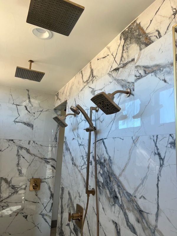 Marble-tiled shower with multiple black showerheads and gold fixtures