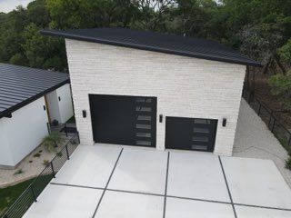 Modern white two-car garage with black doors and a wide concrete driveway, viewed from above