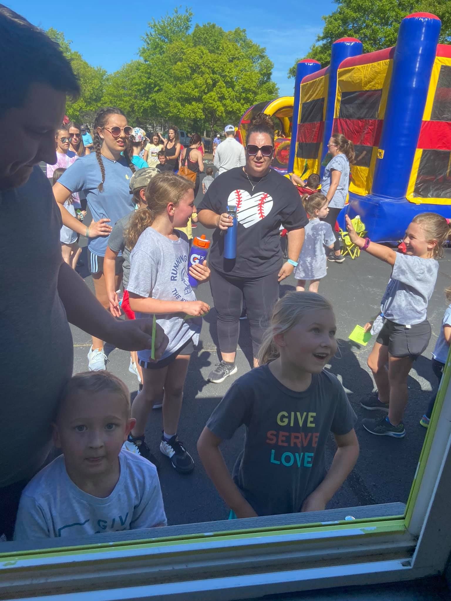 A group of people gathers outdoors in front of an inflatable bounce house on a sunny day.