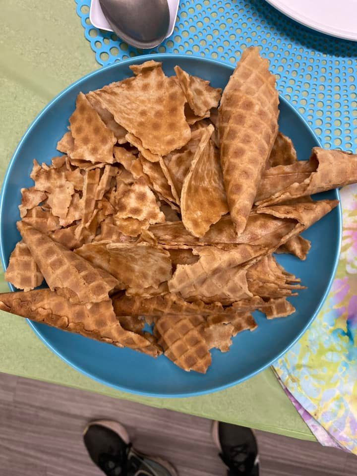 A blue plate piled with broken pieces and rolled cones of crispy brown waffle-style cookies.