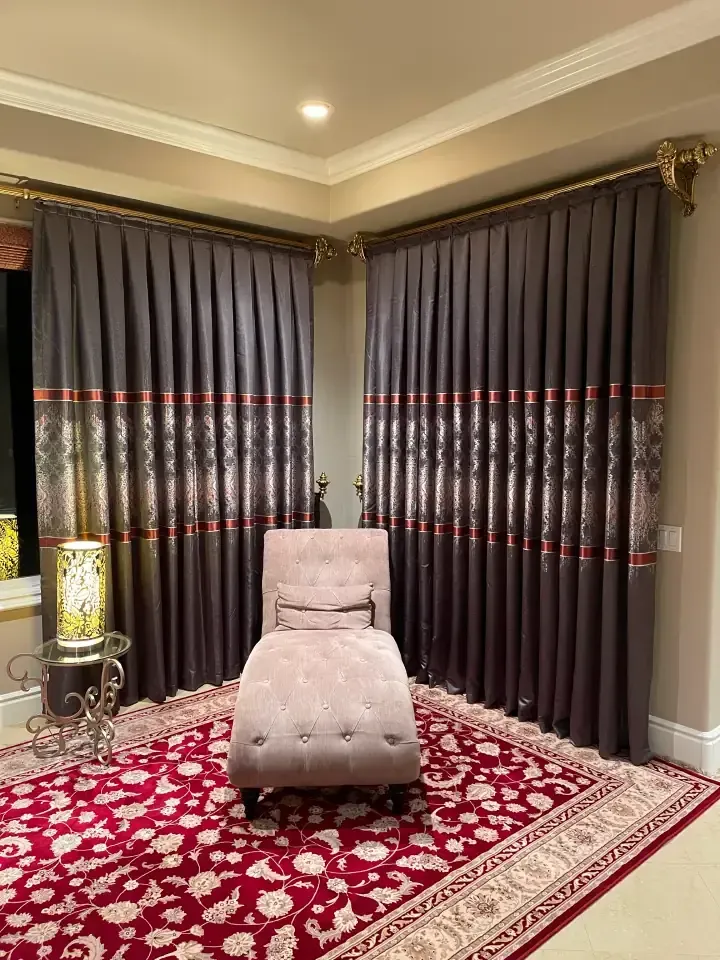 There is a chair and a rug in the room with large dark curtains.