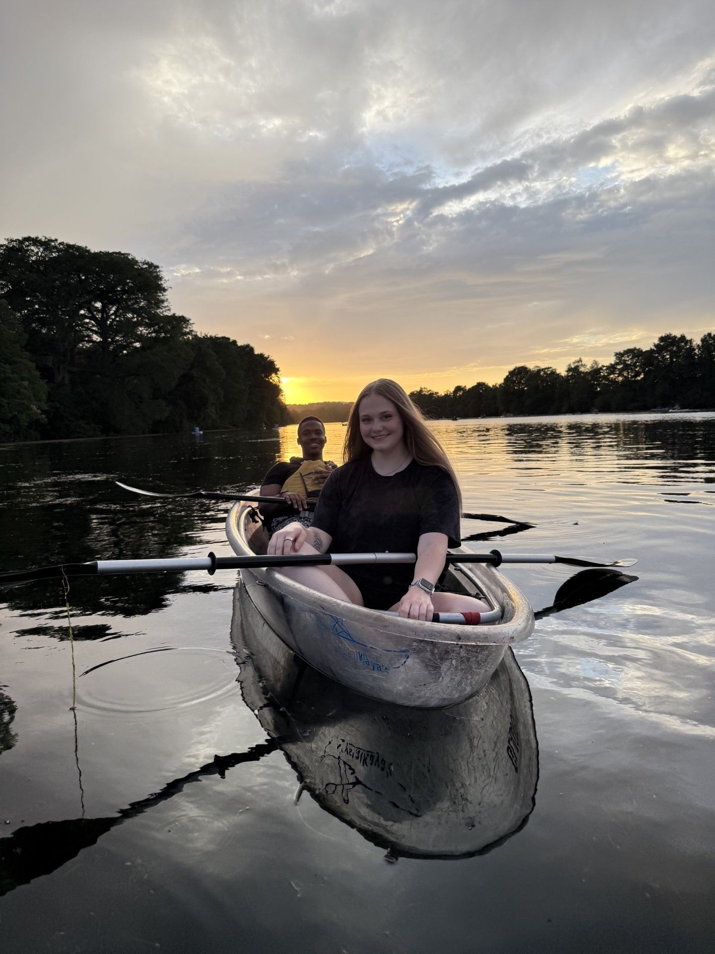 Woman kayaking on a lake at sunset, another person in the background, calm water reflecting the sky.