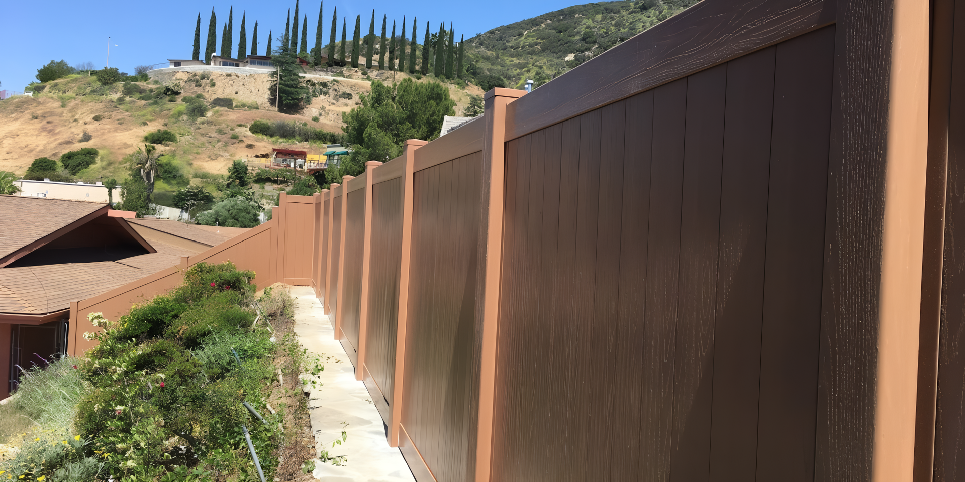 Brown privacy fence on a residential property with a view of a hillside and blue sky.