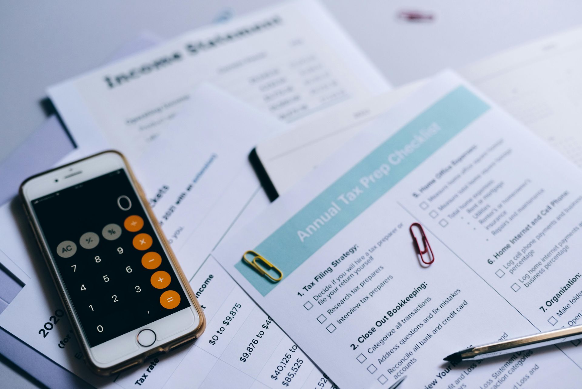 Phone with calculator app and tax documents including an income statement and checklist.
