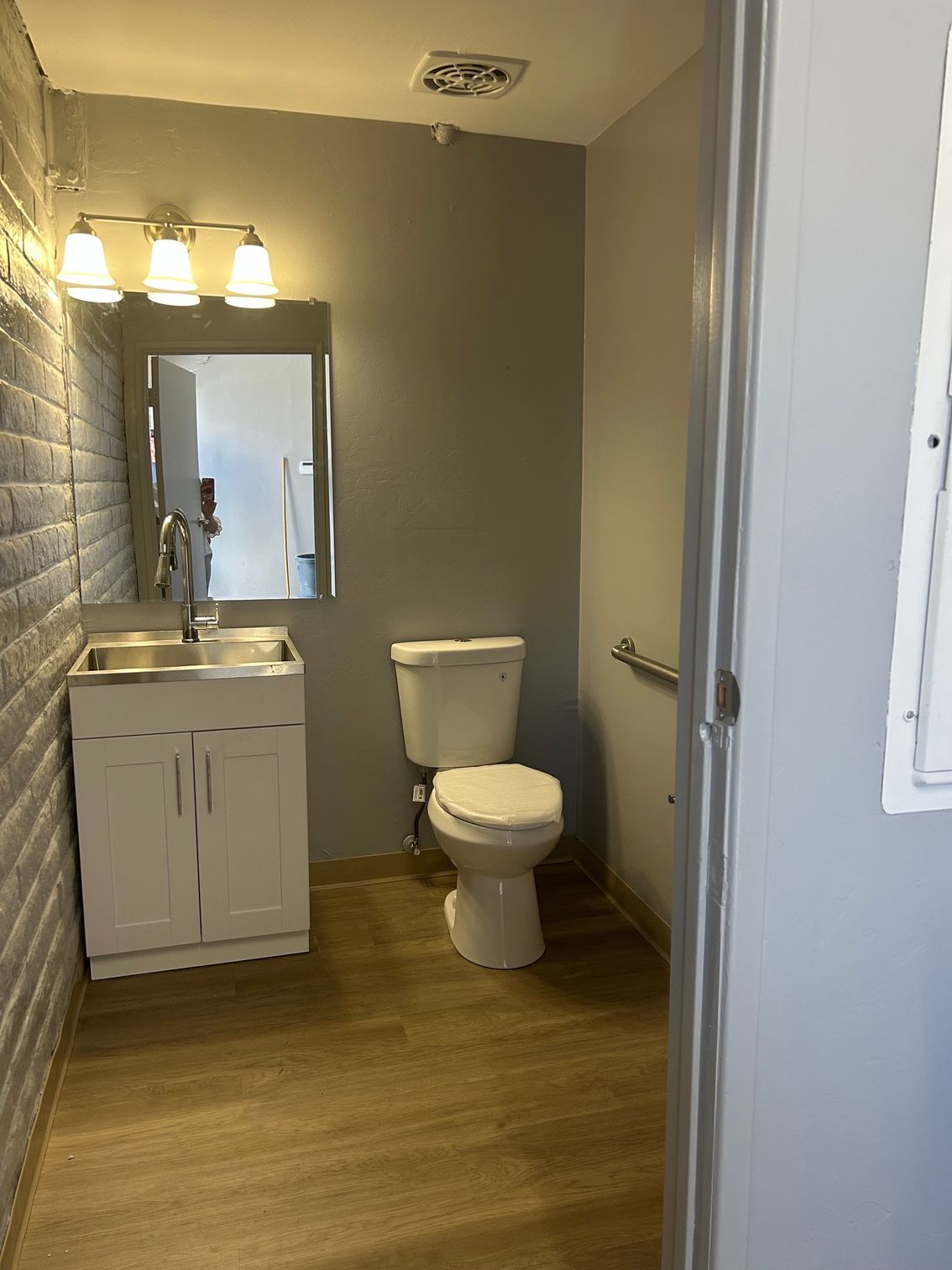 Small bathroom with a toilet, white sink vanity, mirror, and wood-look floor.