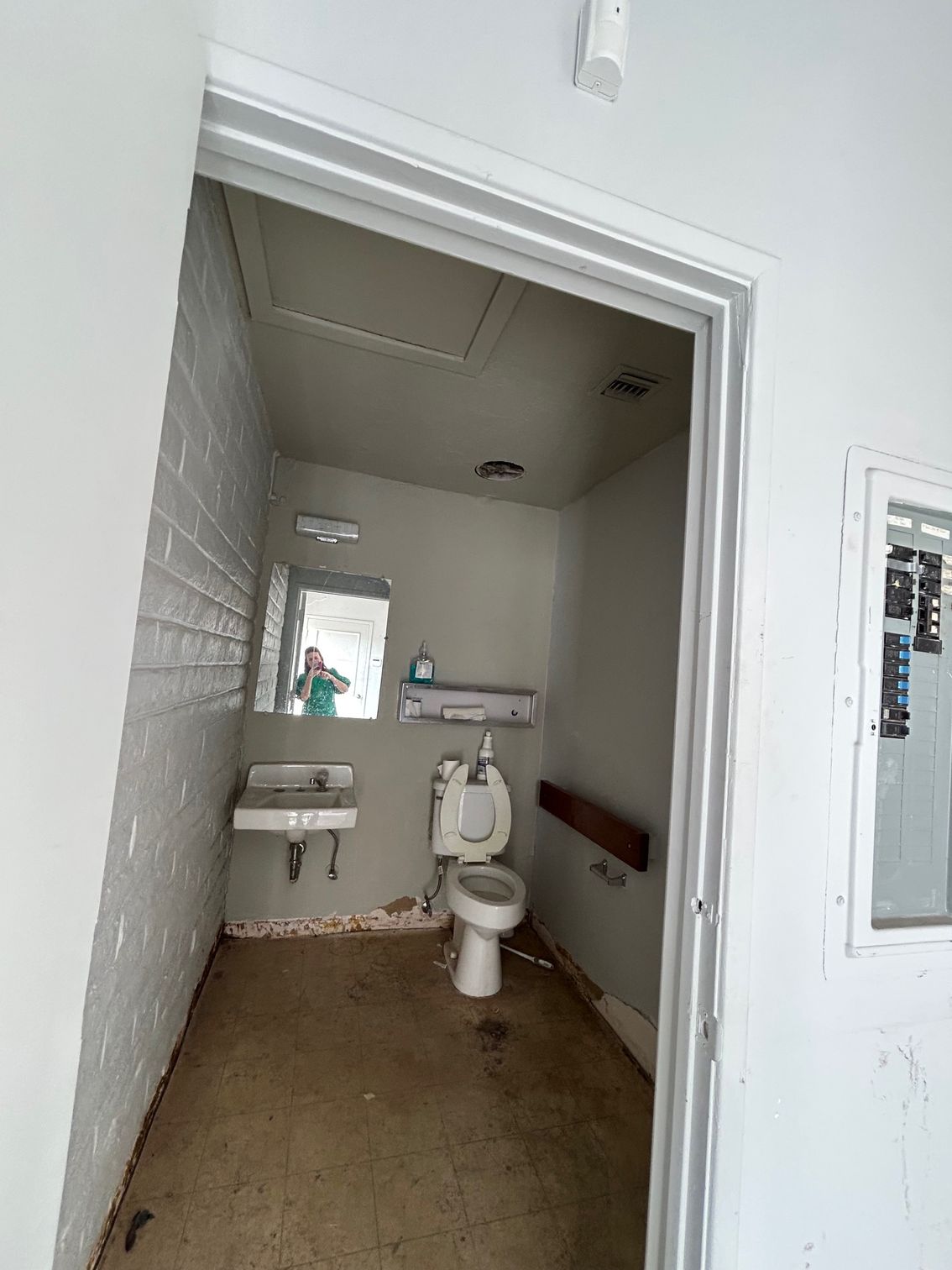 Small public restroom with a toilet, sink, and mirror in a white-walled room.