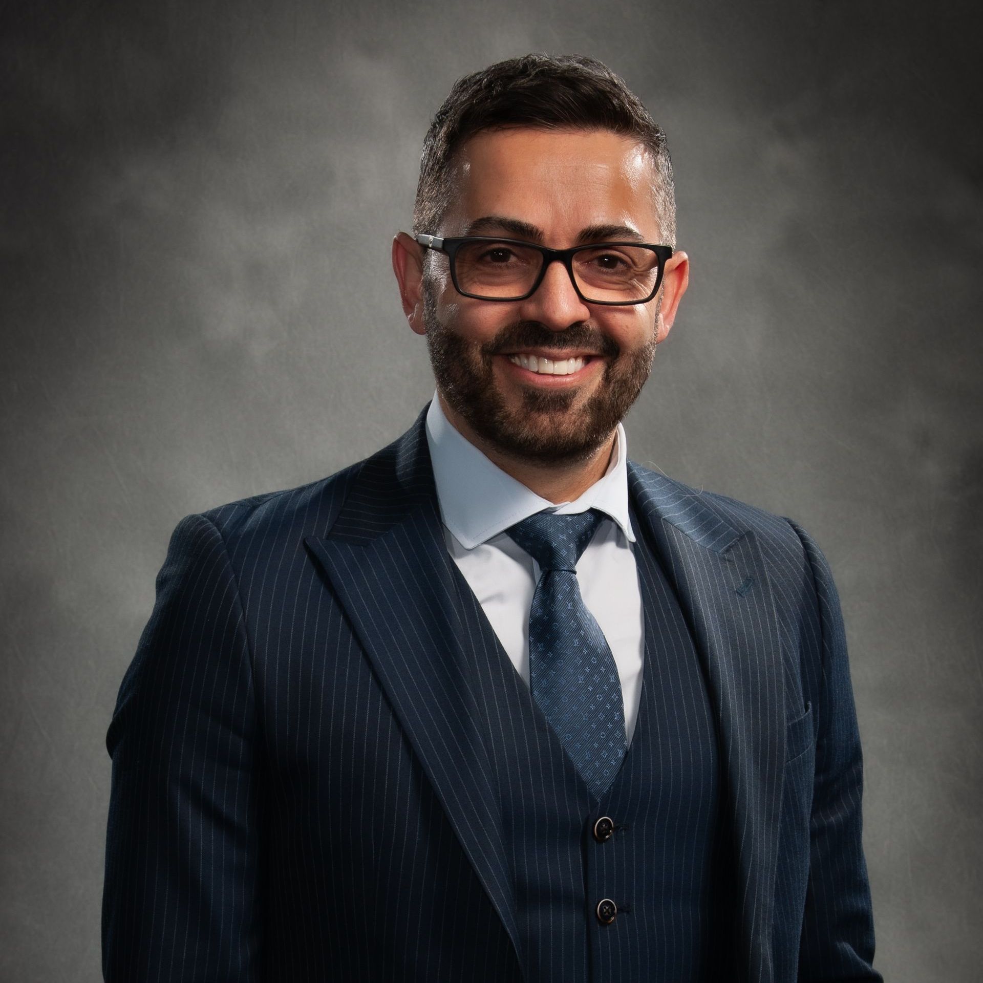 Man in a navy suit and tie smiling against a gray studio background