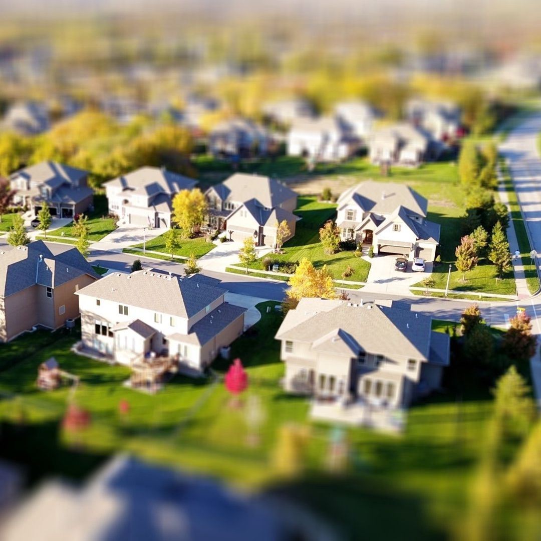 Tilt-shift aerial view of a suburban neighborhood with rows of houses and green yards