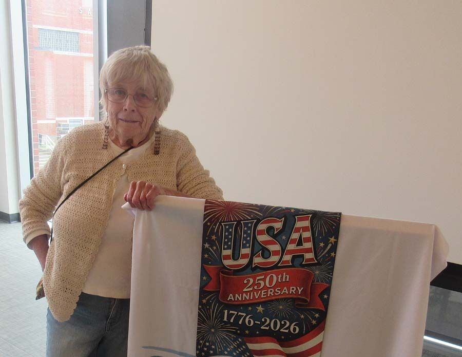 Woman standing beside a table holding a USA 250th anniversary banner