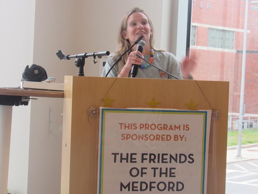 Woman speaking at a podium with a sign reading “The Friends of the Medford...”