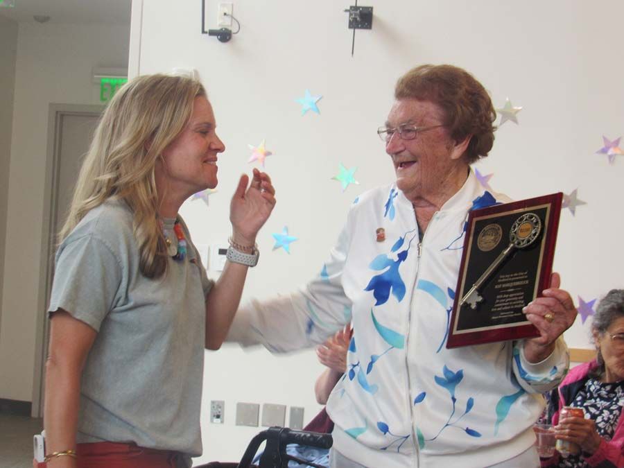 Two women smiling during an award presentation, one holding a plaque and the other receiving it.