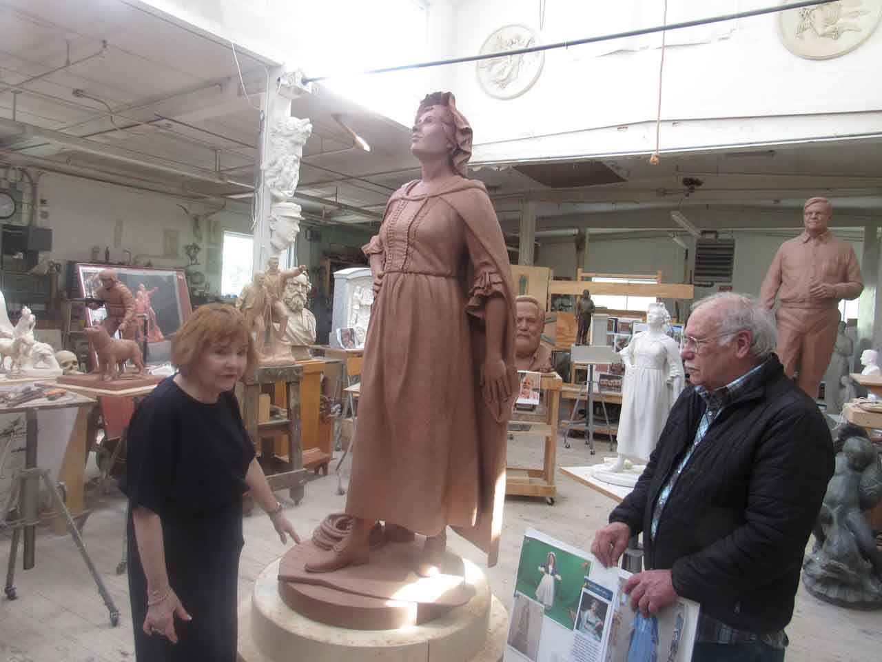 Two people in a sculpture studio, admiring a clay statue of a woman.