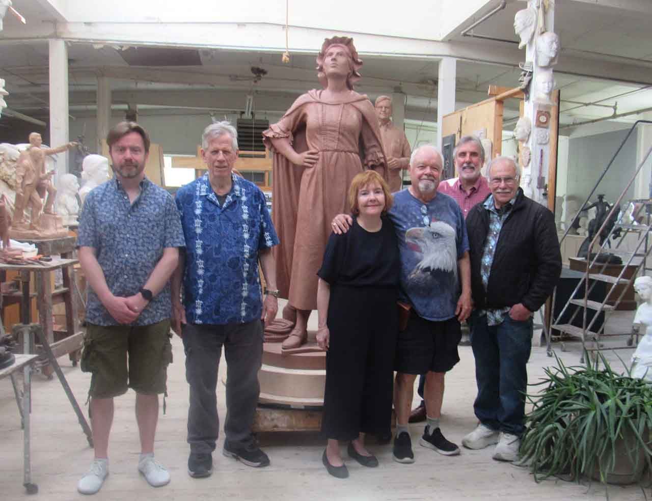 Group of people pose with a clay statue in a studio. The statue depicts a woman.
