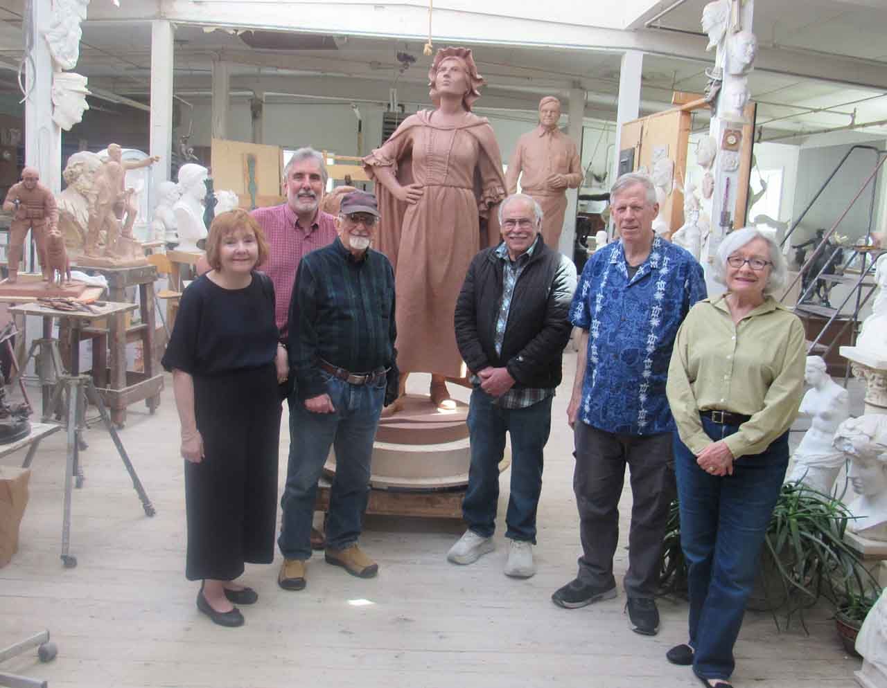 Group of people with a bronze statue of a woman in an art studio.