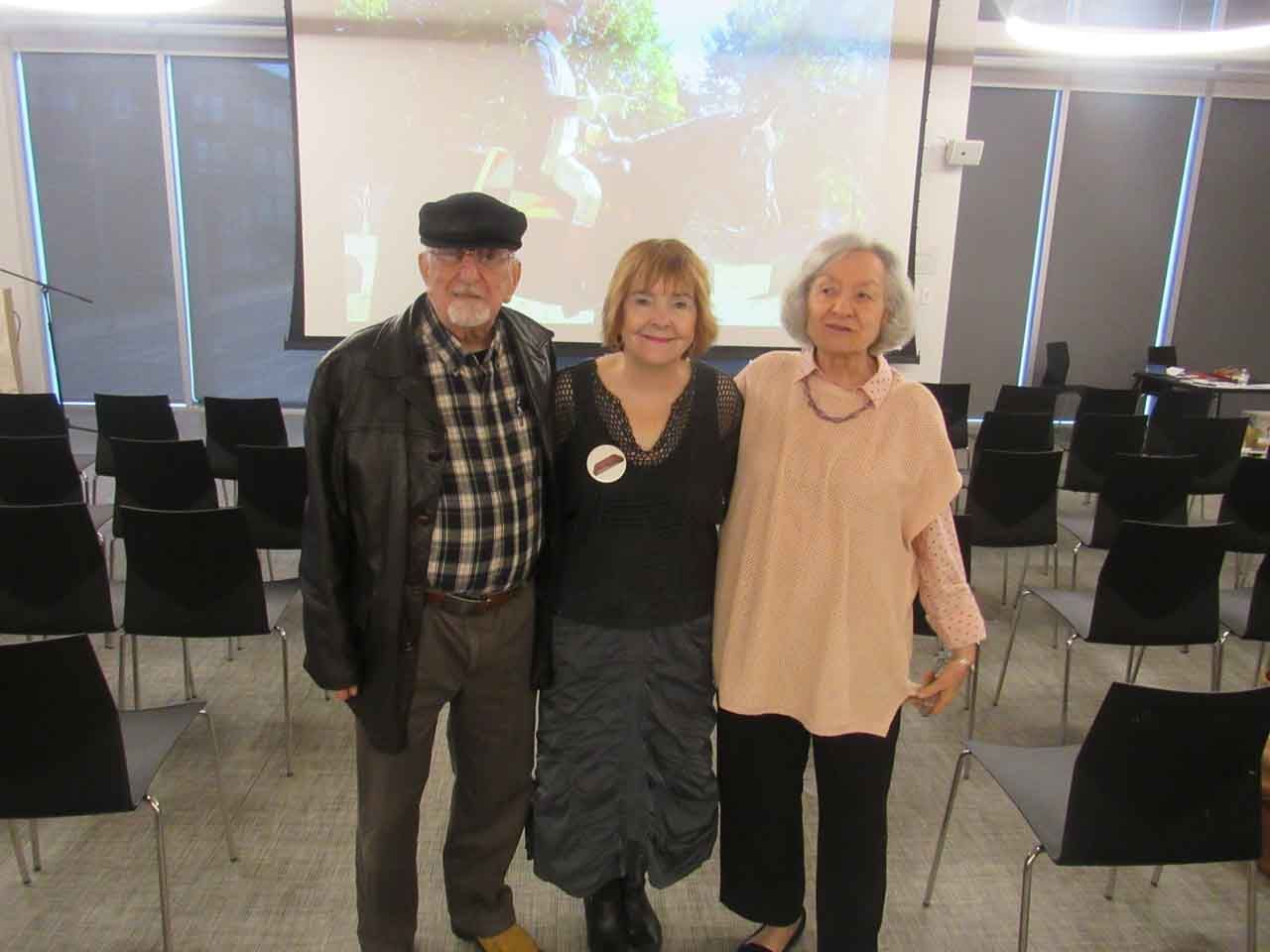 Three people pose in front of a screen and rows of chairs. The people are smiling.