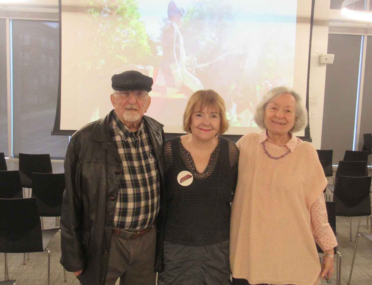 Three people, arms around each other, pose in front of a projector screen.