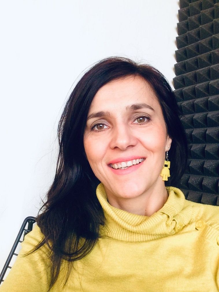 Žena s tmavými vlasy, usmívající se ve žlutém svetru na světlém pozadí