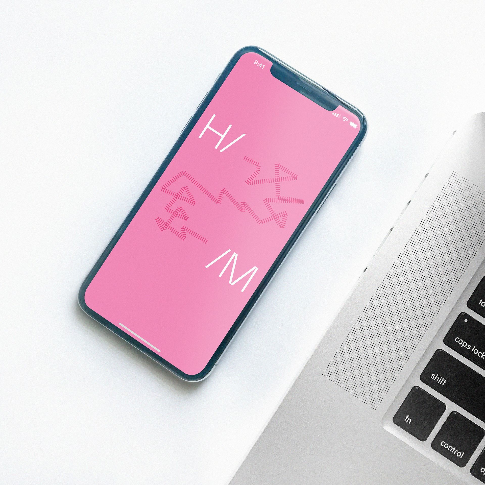 Růžový smartphone s nápisem „Ahoj“ na obrazovce vedle notebooku na bílém stole