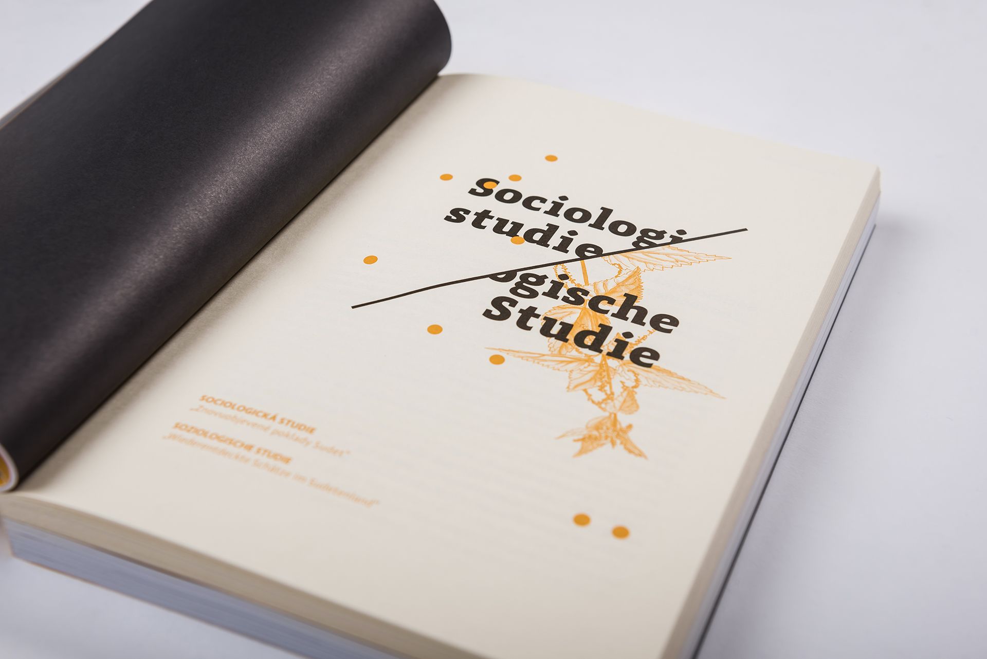 Otevřená studijní brožura ze sociologie s černým obalem na bílém stole