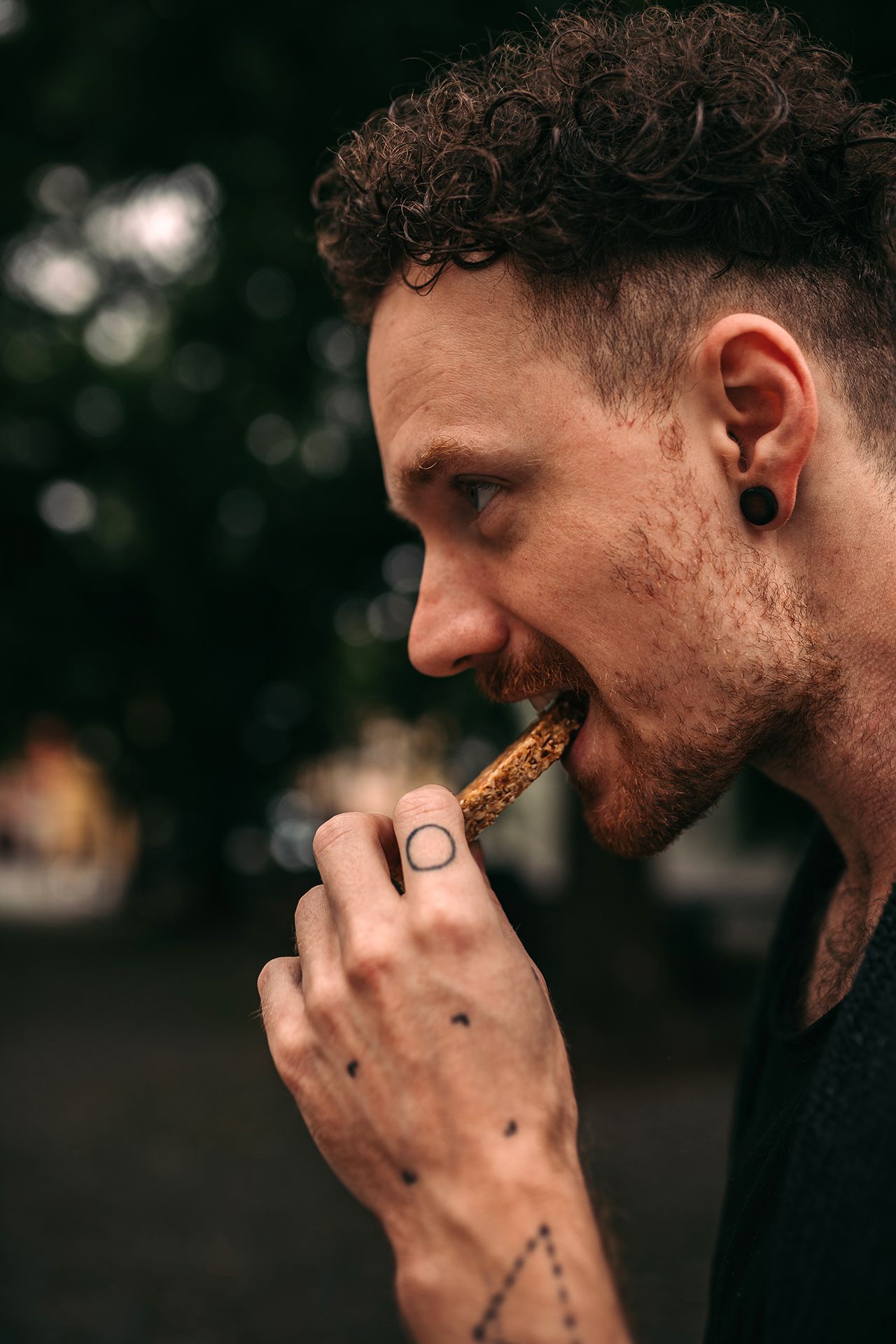 Detailní záběr osoby kouřící cigaretu venku s rozmazanými stromy v pozadí.