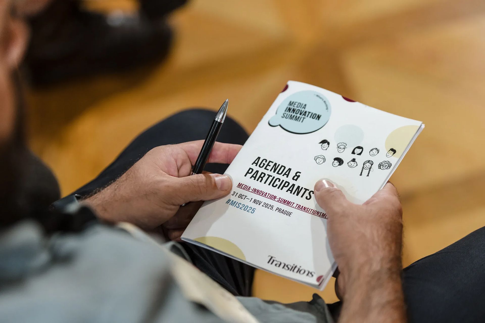 Ruce držící brožuru a pero na židli a čtou text o akci na podporu a účast.