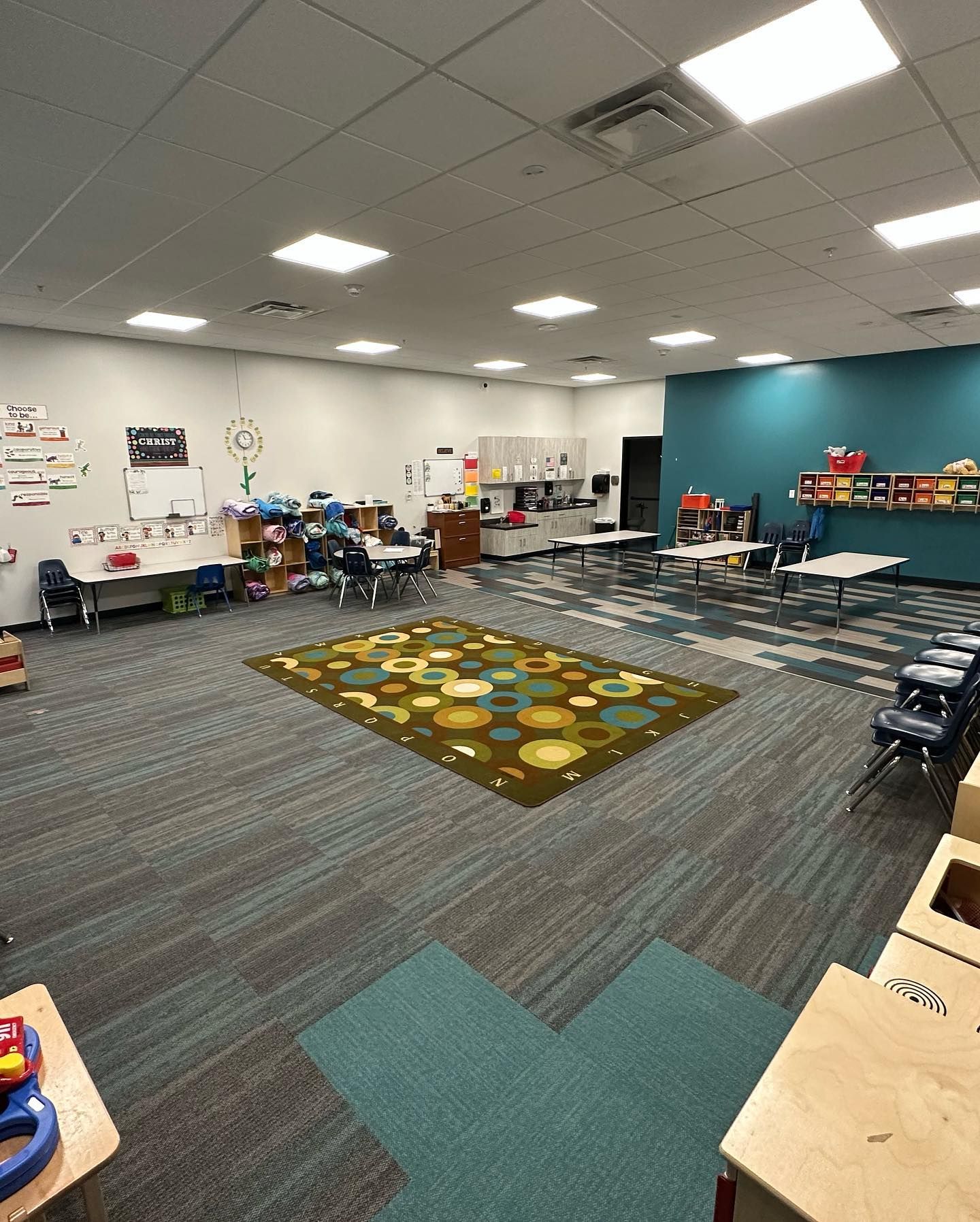 A large classroom with tables and chairs and a rug on the floor.