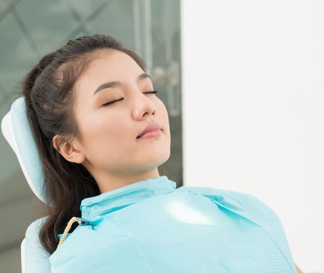 A woman is laying in a dental chair with her eyes closed.