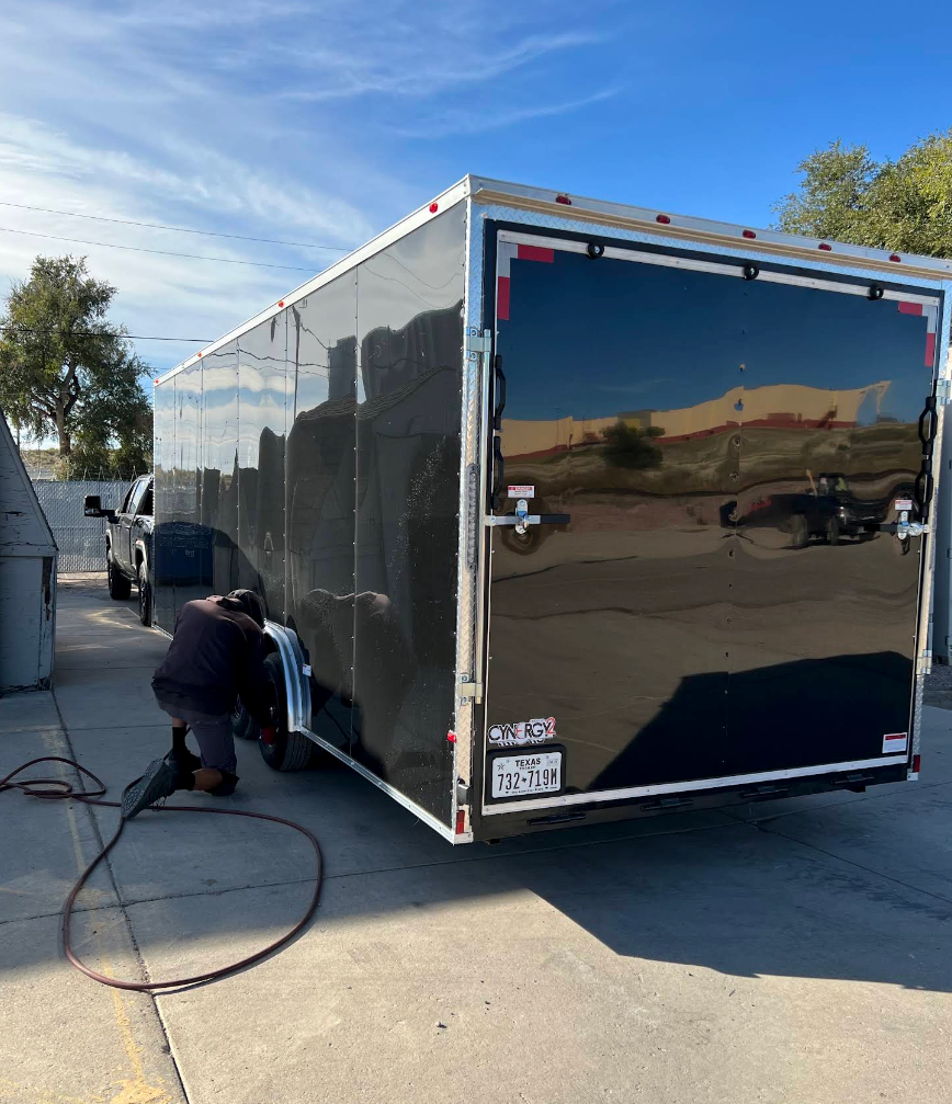 Person kneels beside a black enclosed trailer, attaching cables in a parking lot. | Colorado Tire Auto Care Center