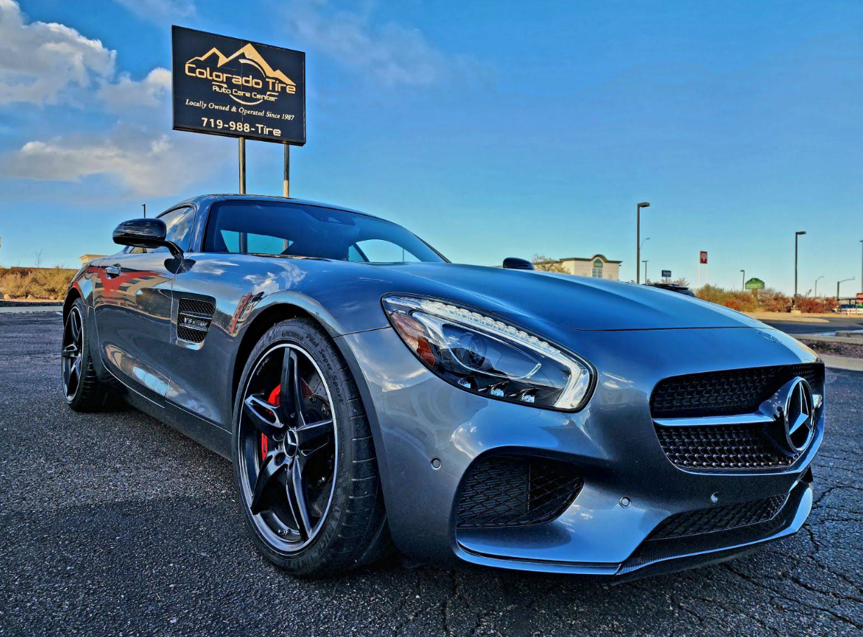 Silver sports car parked outdoors under a blue sky, front three-quarter view with dealership sign behind it | Colorado Tire Auto Care Center