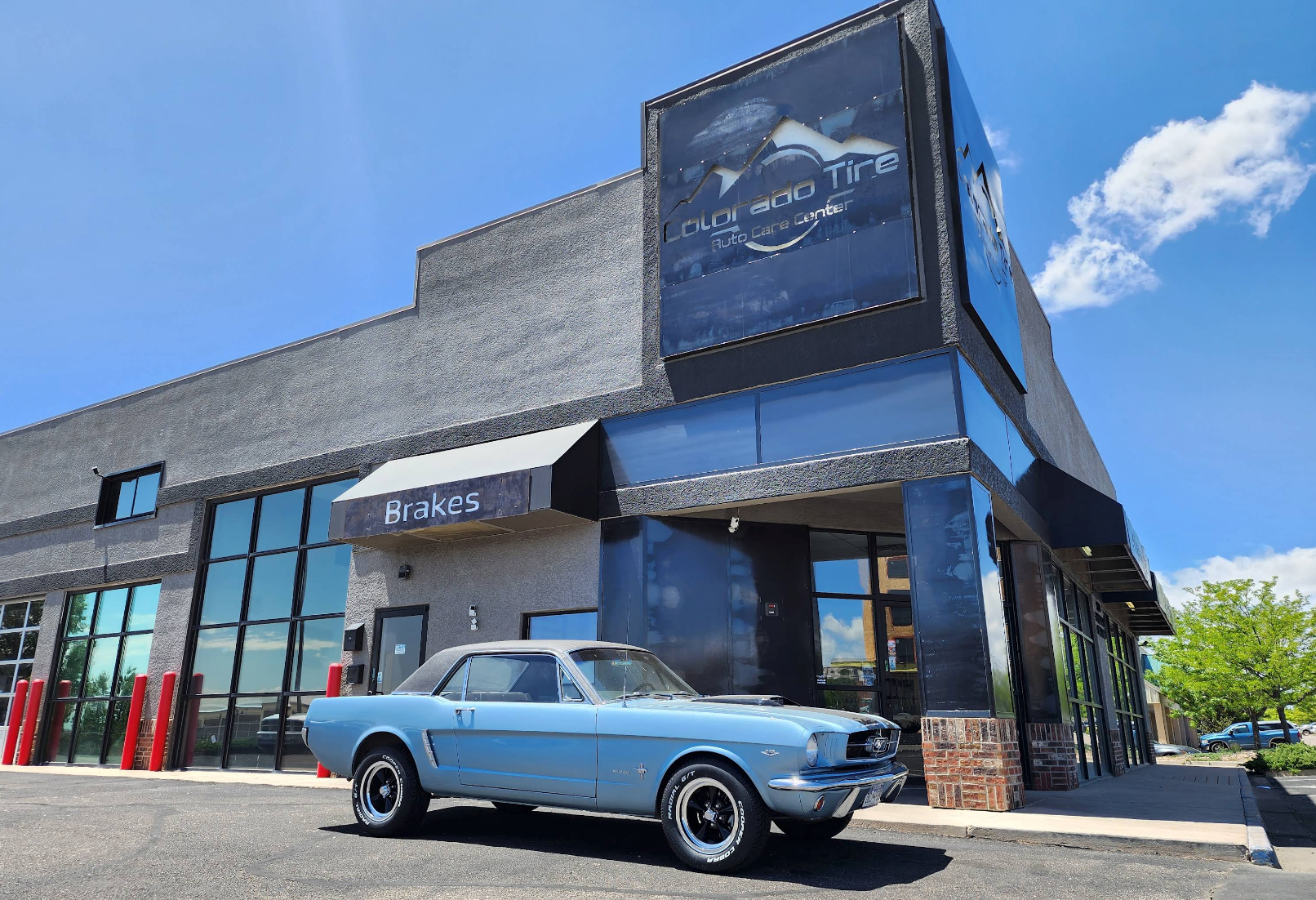 Classic light blue convertible parked outside a modern storefront under a bright blue sky. | Colorado Tire Auto Care Center