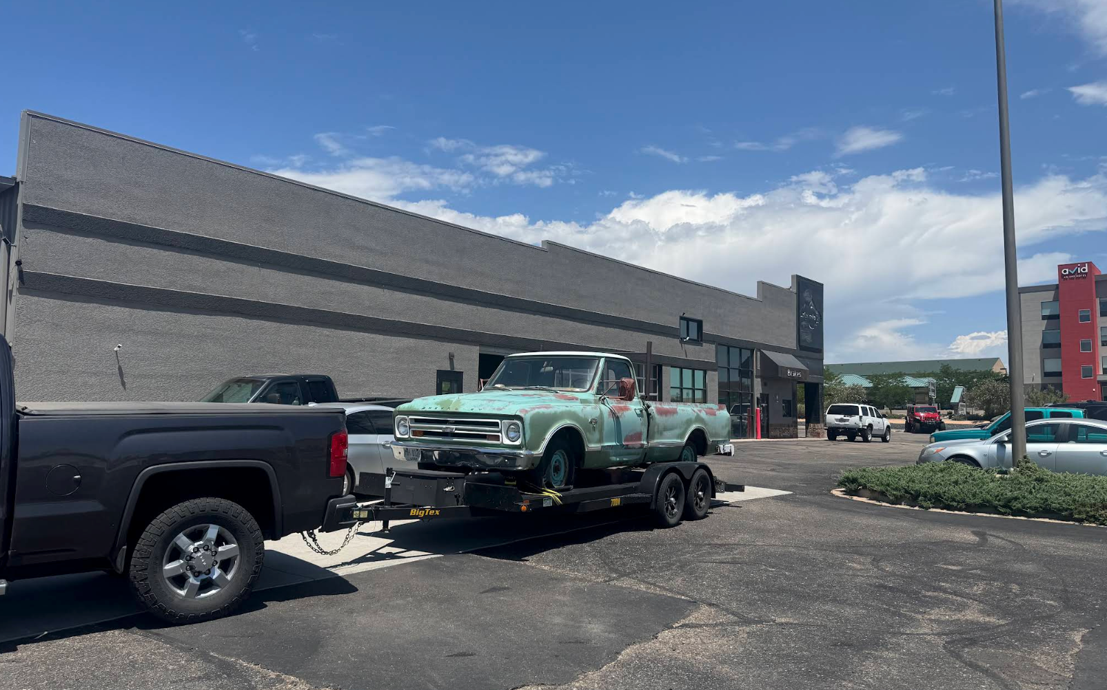 Green vintage pickup on a car carrier beside a store parking lot under a blue sky | Colorado Tire Auto Care Center