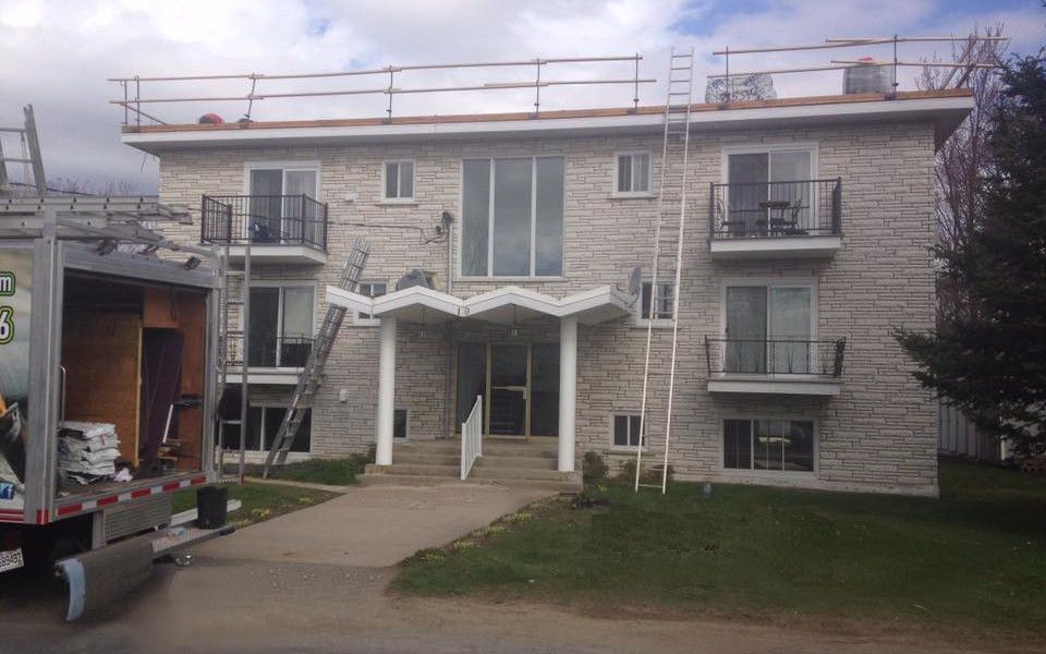 Immeuble d'appartements à façade en pierre, travaux de toiture en cours ; camion et échelles présents.