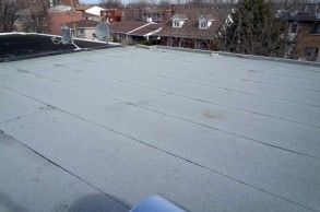 Toit plat gris avec joints apparents, maisons en arrière-plan.