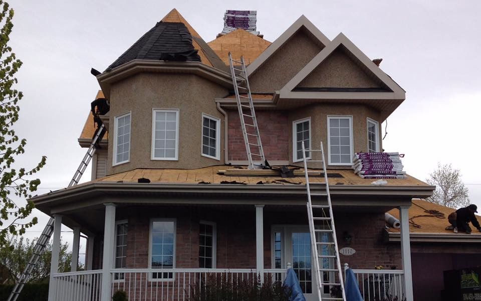 Des ouvriers sur des échelles remplacent les tuiles du toit d'une maison en briques de deux étages.