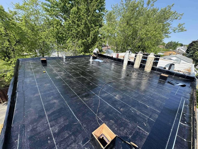 Toit plat argenté d'un bâtiment commercial sous un ciel bleu, avec des finitions blanches et un aperçu des bâtiments environnants.