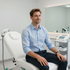 Man in a light blue shirt seated in a white medical clinic chair, smiling in a bright treatment room