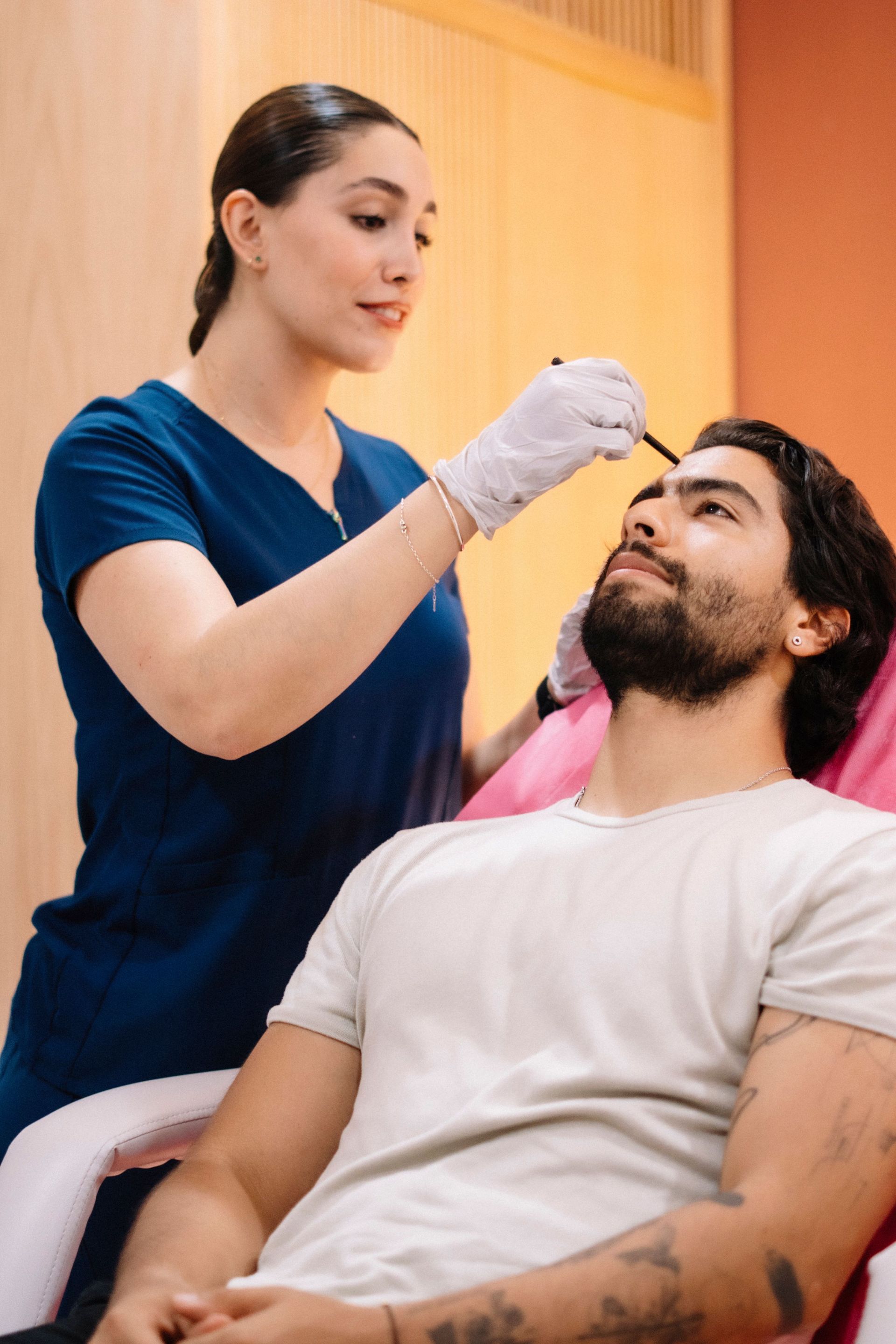 Clinician applying eyebrow treatment to reclining man in a clinic chair