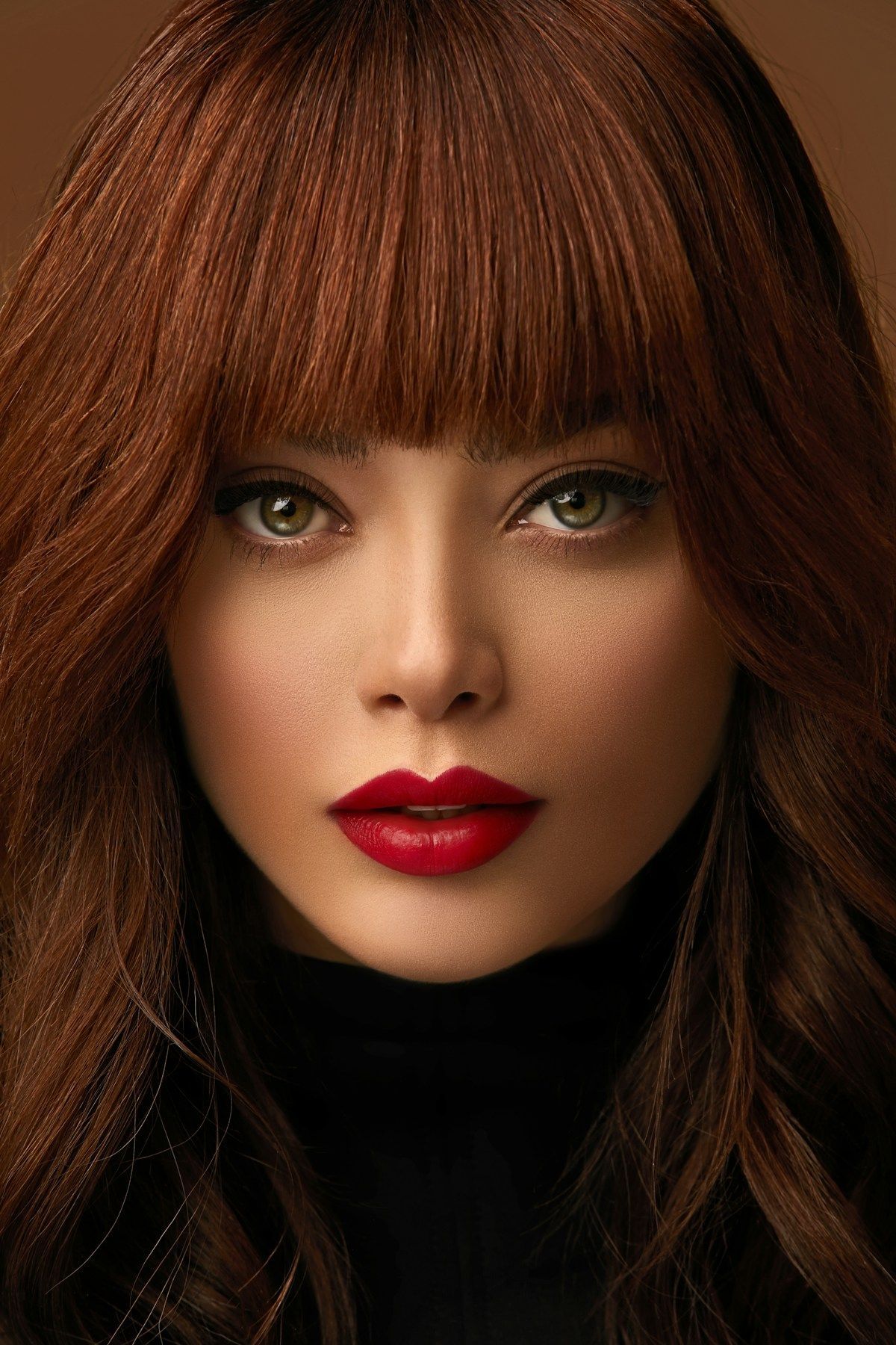 Close-up portrait of a person with auburn hair, bangs, red lipstick, and a dark turtleneck against a dark background