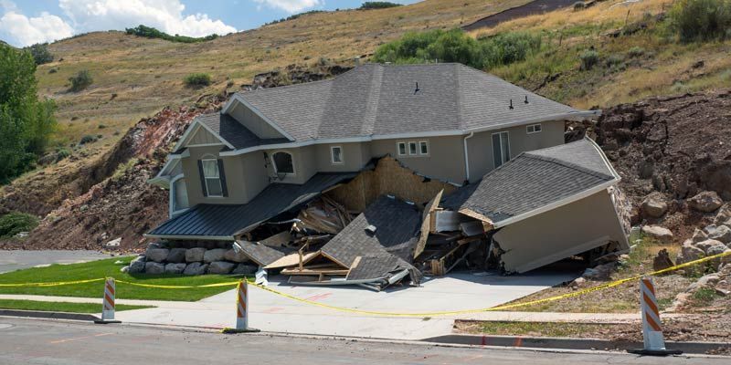 A house is partially destroyed by a landslide. The house is angled and resting on the debris from the hillside.