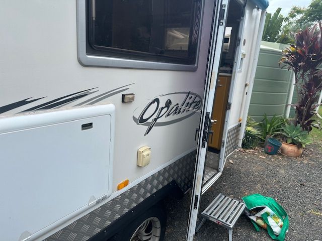 White Opalite caravan with open door, parked outdoors with greenery and water tank visible — Gas Fitting Services in Bundaberg, QLD