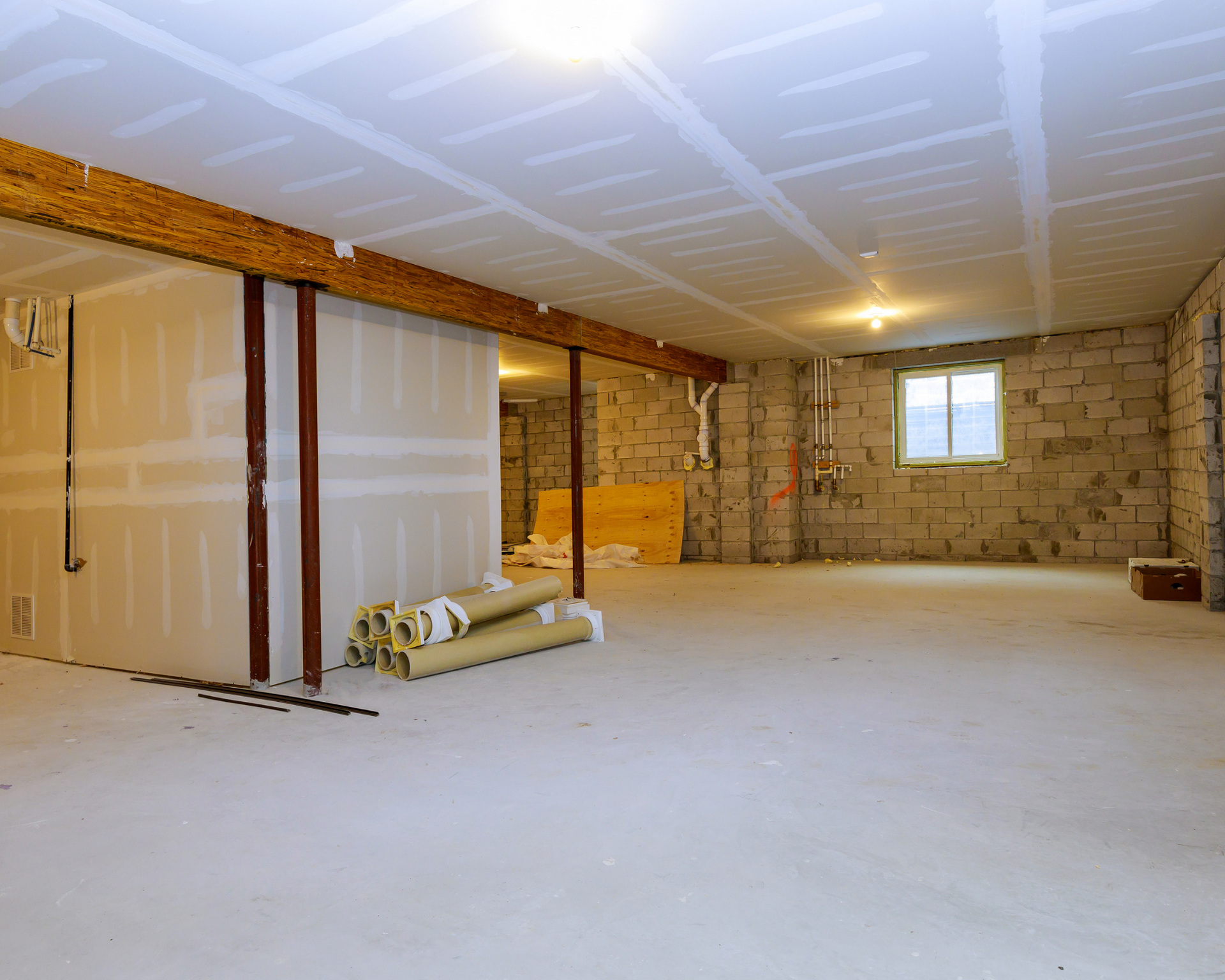 Basement under construction with exposed concrete block walls, drywall, and framing; unfinished flooring and ceiling.