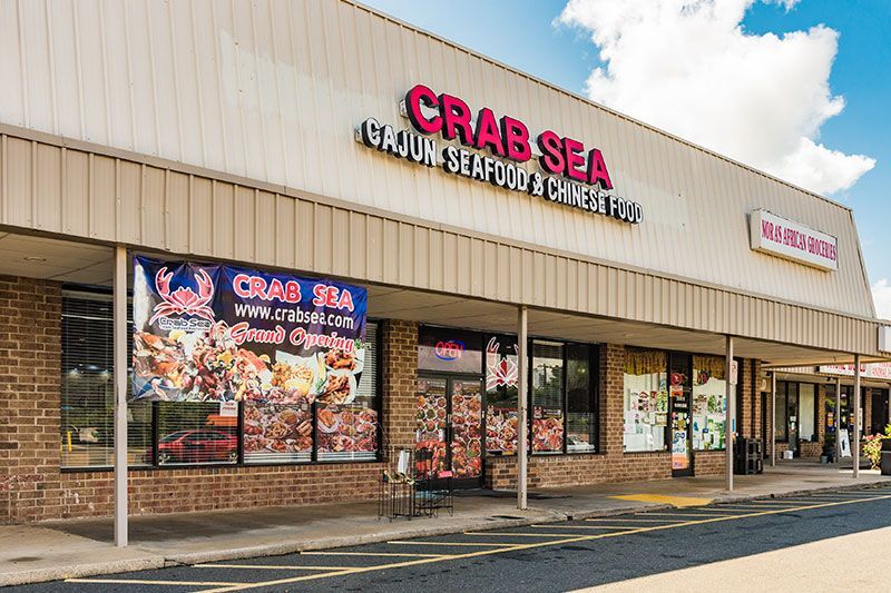 Crab Sea seafood restaurant storefront in a strip mall with red signage and window ads