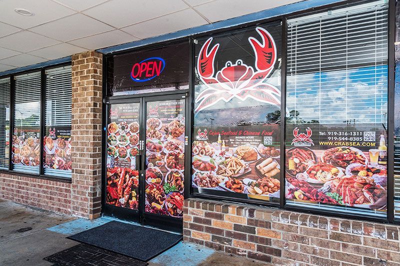 Seafood restaurant storefront with neon “OPEN” sign and crab logo, brick exterior, and window seafood photos