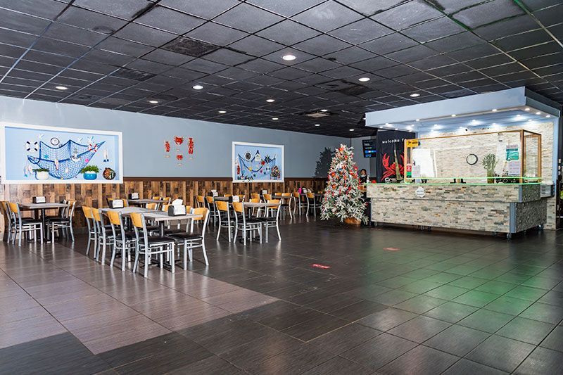 Spacious cafeteria with tables, chairs, wall art, and a decorated Christmas tree near the counter.