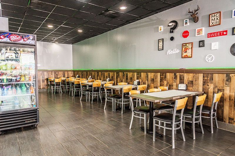 Empty restaurant dining area with rows of tables and chairs, dark tile floor, and a refrigerator display on the left
